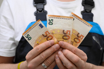 Pracownik fizyczny branży budowlanej trzyma w dłoniach banknoty euro