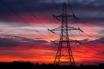 Electricity pylons and high voltage power lines with colourful sunrise in clouds