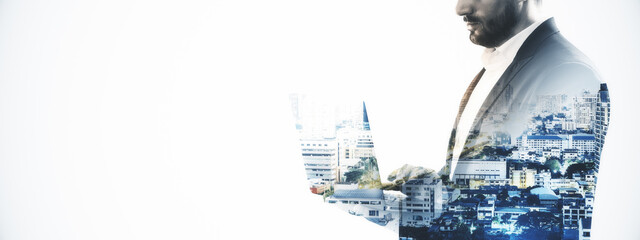 Businessman using laptop with cityscape overlay on light background representing modern urban business concept.