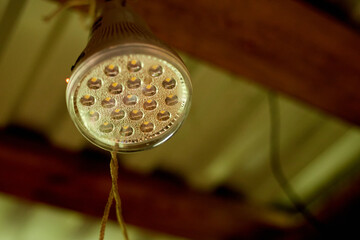 A white street lamp with its bulb turned off, hanging on a dark green wooden crowbar, next to long garlands with white round bulbs.