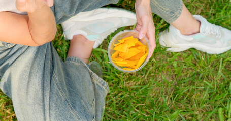 Close-up of a girl picking dried mango from a container in the park.