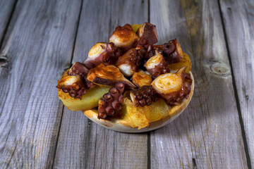 Galician-style octopus tapa on a rustic wooden table, bathed in oil and paprika, and garnished with potatoes.