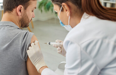 Obraz premium Nurse or doctor giving injection in the shoulder to male patient in clinic to prevent pandemic. Man receiving a dose of vaccine in medical center or hospital. Vaccination and medicine concept.