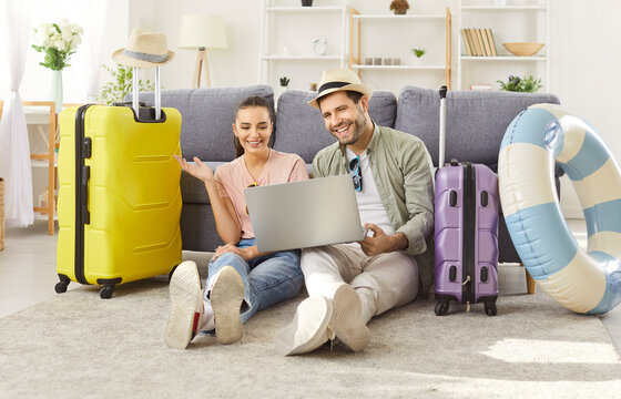Tourist couple planning summer trip online from home with laptop happy packing luggage bag for traveling, vacation trip, big suitcase for honeymoon, dreaming, wearing summer trip holiday beach wear