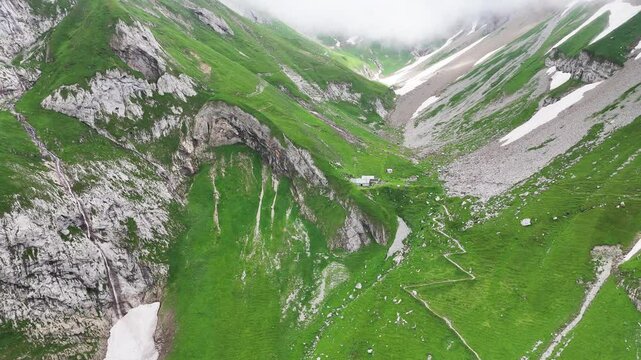 9 juli 2024, Wildhaus, Switzerland. backward Drone flight, zooming out from old mountain hut Schafboden, build on green Alpstein mountains.  Stunning scenery, great outdoors. Some snow in mountains.