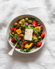 Traditional Greek salad with fresh vegetables, arugula and feta cheese on a light background, top view