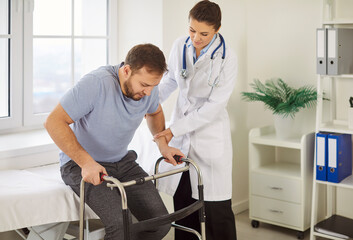 Friendly female doctor assisting male patient with walkers in medical office. Disabled young man...