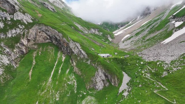 9 juli 2024, Wildhaus, Switzerland. Forward Drone flight, zooming inon old mountain hut Schafboden, build on green Alpstein mountains.  Stunning scenery, great outdoors. Some snow in mountains.