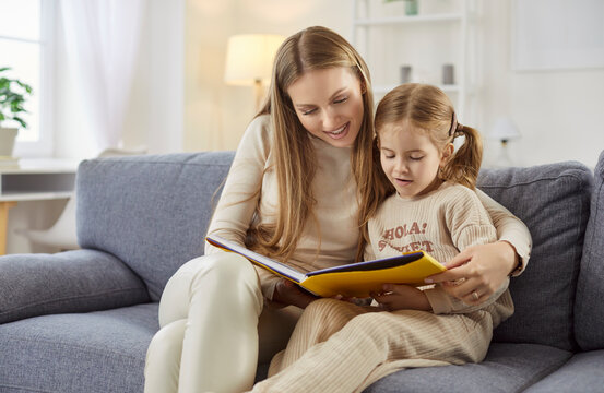 Mother and daughter, family fun at home reading book story, cute little girl, beloved young mom enjoy leisure together time together, sharing close tender moment together, babysitter care service