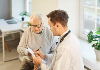 Portrait of a senior elderly gray-haired man patient in medical office listening to male doctor...