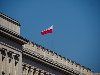 Polish National Flag Waving on Pole Atop Historic Government Building Against Clear Blue Sky