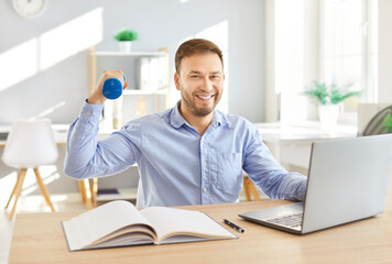 Happy smiling man sitting at desk with laptop, taking break from work, lifting light weight dumbbell. Positive male employee keeping balance between work and sport, integrating workouts into schedule.