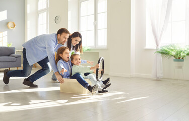 Happy family playing together in living room. Smiling parents pushing their excited children sitting in cardboard box, holding steering wheel and pretending to drive invisible car. Family leisure.