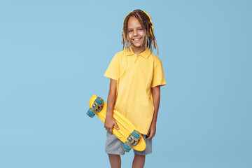 Stylish little boy with african dreads with skateboard on the blue background. Back view.