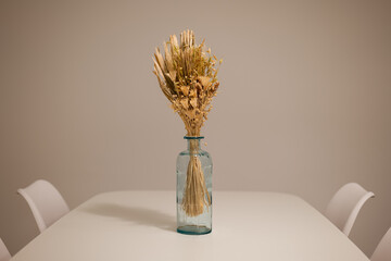 Dining table with white surface and blue glass vase holding dried flowers centered between white chairs