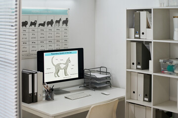 Part of vets office interior with desktop computer on table, posters on wall and shelves with medical records