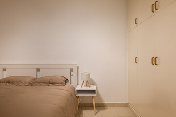 Compact bedroom with taupe bedding, bedside table and integrated wardrobe offering functional storage