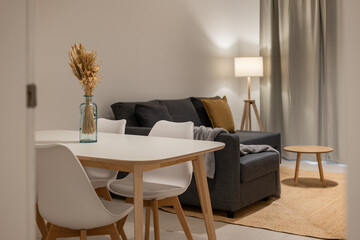 Dining and living room combination with white chairs, blue vase centerpiece, gray sofa and wooden table
