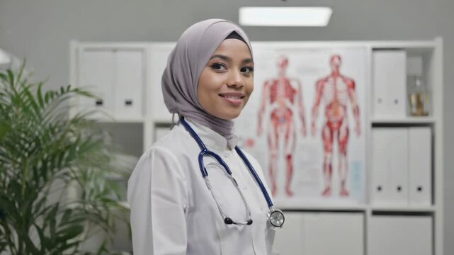 A smiling young female doctor in a medical uniform confidently holds a stethoscope 