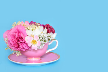 Summer flower arrangement in pink tea cup on blue background. Surreal natural alternative herbal medicine for natural health care. Abstract floral food art design.