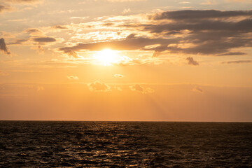 Sunlight reflects off gentle sea waves as the day transitions to evening. The horizon is painted with warm colors, creating a peaceful setting ideal for relaxation and contemplation.