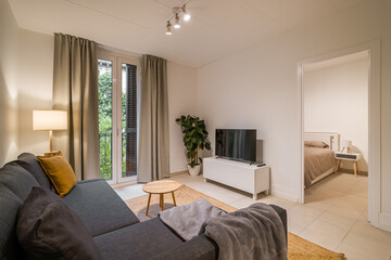 Living room with gray sectional sofa, mustard pillow, TV console, indoor plant and large window with curtains