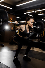 Powerful woman doing squats exercises with heavy barbell in the gym