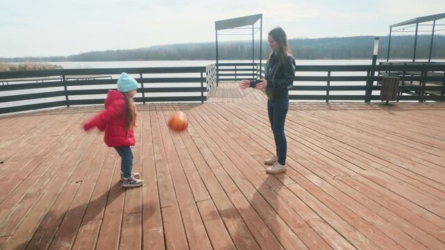 Mother and daughter having fun with ball at the pier near the lake
