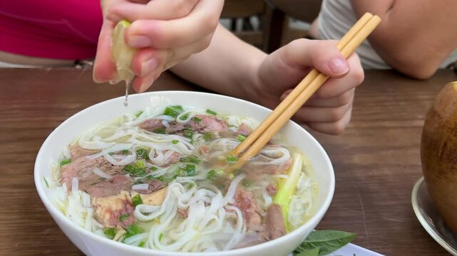 squeeze into lime soup hand squeezes lime over a bowl of pho in a bustling Bangkok restaurant, enhancing the dish's flavor
