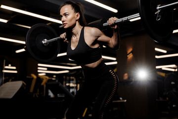 Powerful woman doing squats exercises with heavy barbell in the gym
