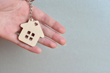 Close-up of a keychain in the shape of a house in hands. Gray background.