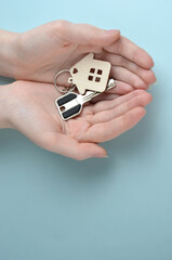 A wooden keychain in the shape of a house and a key in your hands. Blue background.