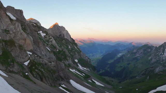 9 juli 2024, Wildhaus, Switzerland. Forward turn, Drone flight, during sunrise in Alpstein mountains. Impressive mountains with some snow, amazing purple, red and orange colors during sunrise. Wonderf