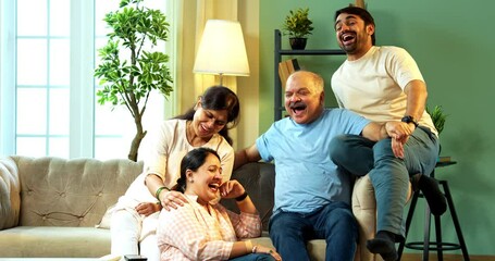 Laughing together while sitting indoors, happy Indian family with senior parents and young adult children enjoying funny conversation on sofa in modern cozy home living room, spending quality time