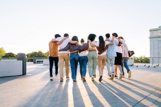 Diverse group of students walking together on a campus rooftop, arms around each other, celebrating friendship and unity against a sunset backdrop