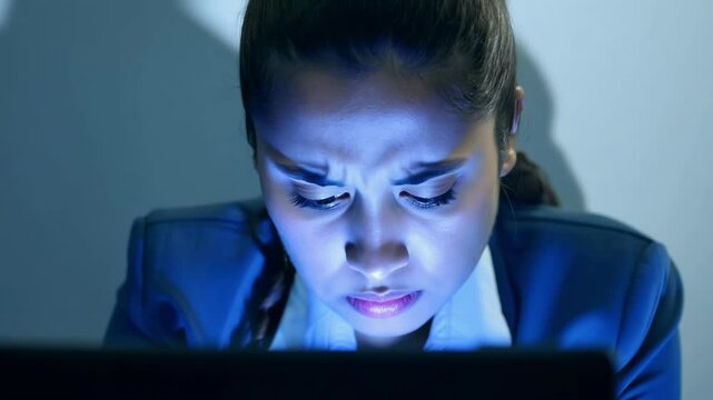 Young woman with focused expression illuminated by blue light from screen. Her face shows shifting emotions as she intently watches something concerning, with light reflecting off her features.