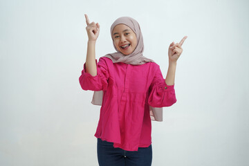Smiling Young Asian Muslim Woman in Hijab Pointing with Both Hands on isolated background