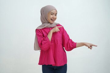 Smiling Young Asian Muslim Woman in Hijab Pointing with Both Hands on isolated background