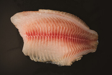 Fresh tilapia fillet on black background, top view.