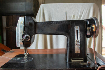 Frontal view of an antique black sewing machine placed on a wooden surface. Shows mechanical elegance and design from a bygone era, ideal for vintage industry themes.
