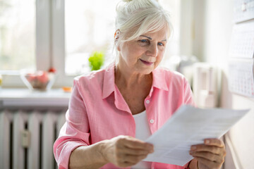 Senior woman looking through financial documents at home 

