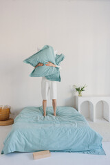 A person is holding two fluffy pillows high above their head while playfully standing on a comfortable bed that is neatly made