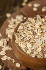 wooden bowl with oatmeal flakes for making porridge, scattered dry cereal flakes from oats, flattened, steamed and dried, closeup