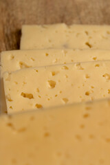 a piece of semi-hard cheese with holes in place of slicing for cooking, pieces of sliced cheese on a board, close up