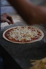 Sprinkling cheese on a pizza base with tomato sauce