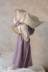 A woman is wearing a beautiful purple dress while skillfully balancing a large pile of colorful pillows on her head with great poise
