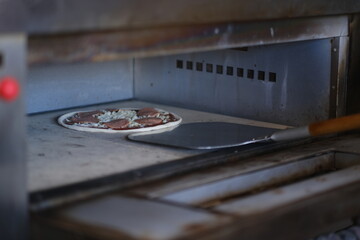 Pepperoni pizza placed in the oven with a metal pizza peel