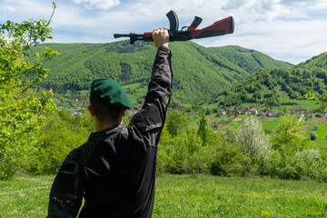 Camouflaged soldier in green beret observing through binoculars in bright green forest terrain.