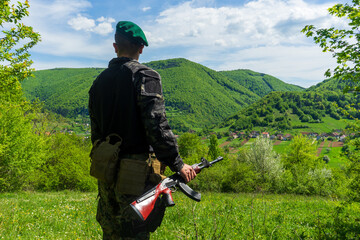 Soldier in green beret overlooking and celebrating victory over a town in bright green forest...