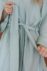 A woman is currently wearing a light blue robe that has a tie neatly wrapped around her waist, adding a stylish touch to her appearance